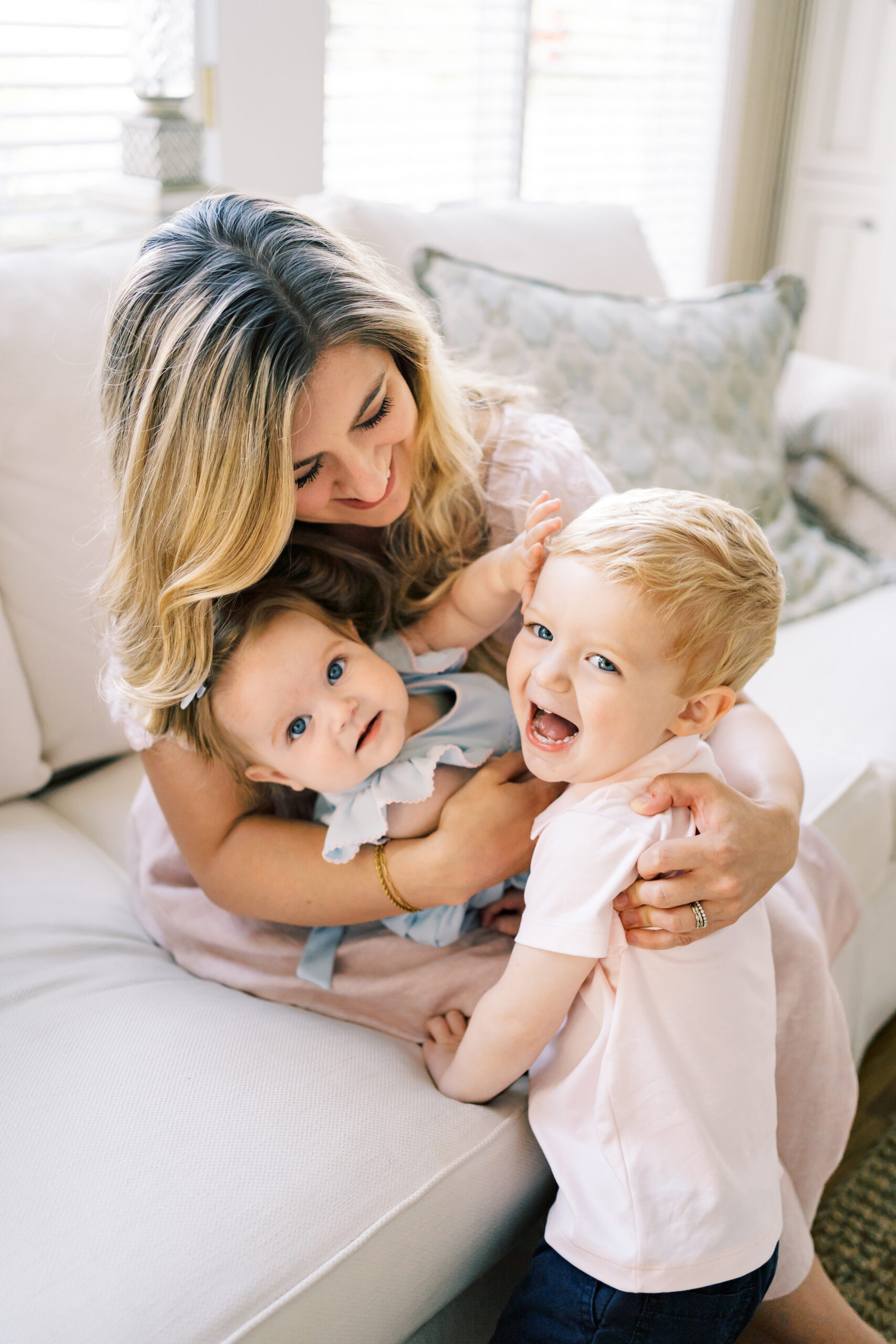 An infant in mom's lap reaches for laughing big brother while on a couch after visiting The Lili Pad